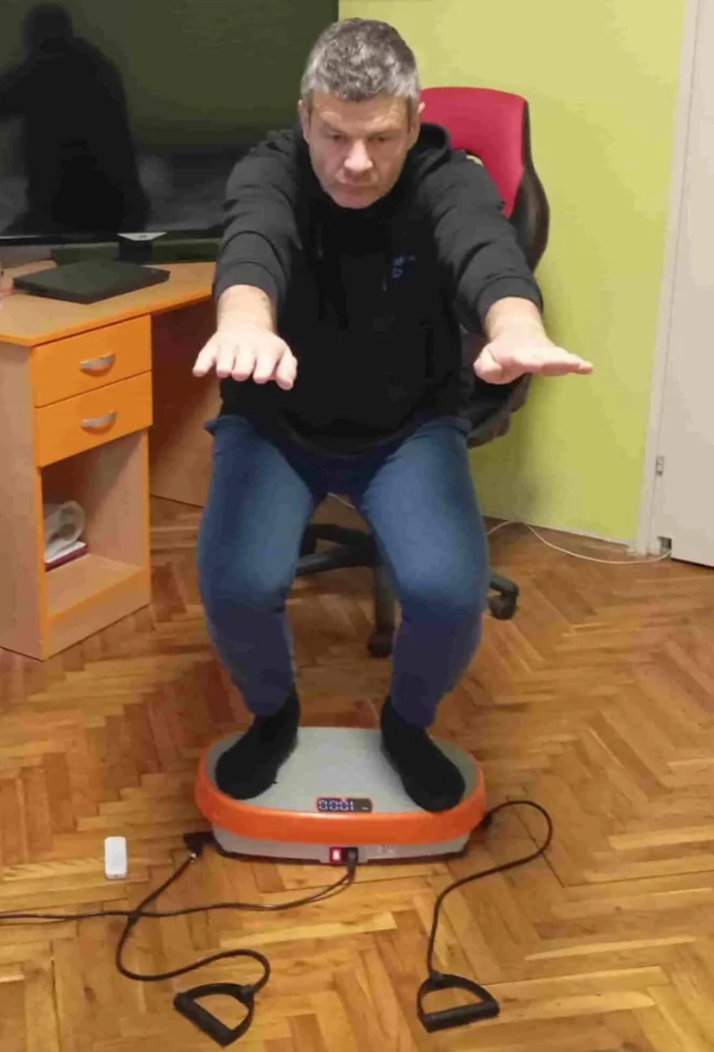 Vladimir Stanar on a vibration plate in a deeper half squat arms outstreched