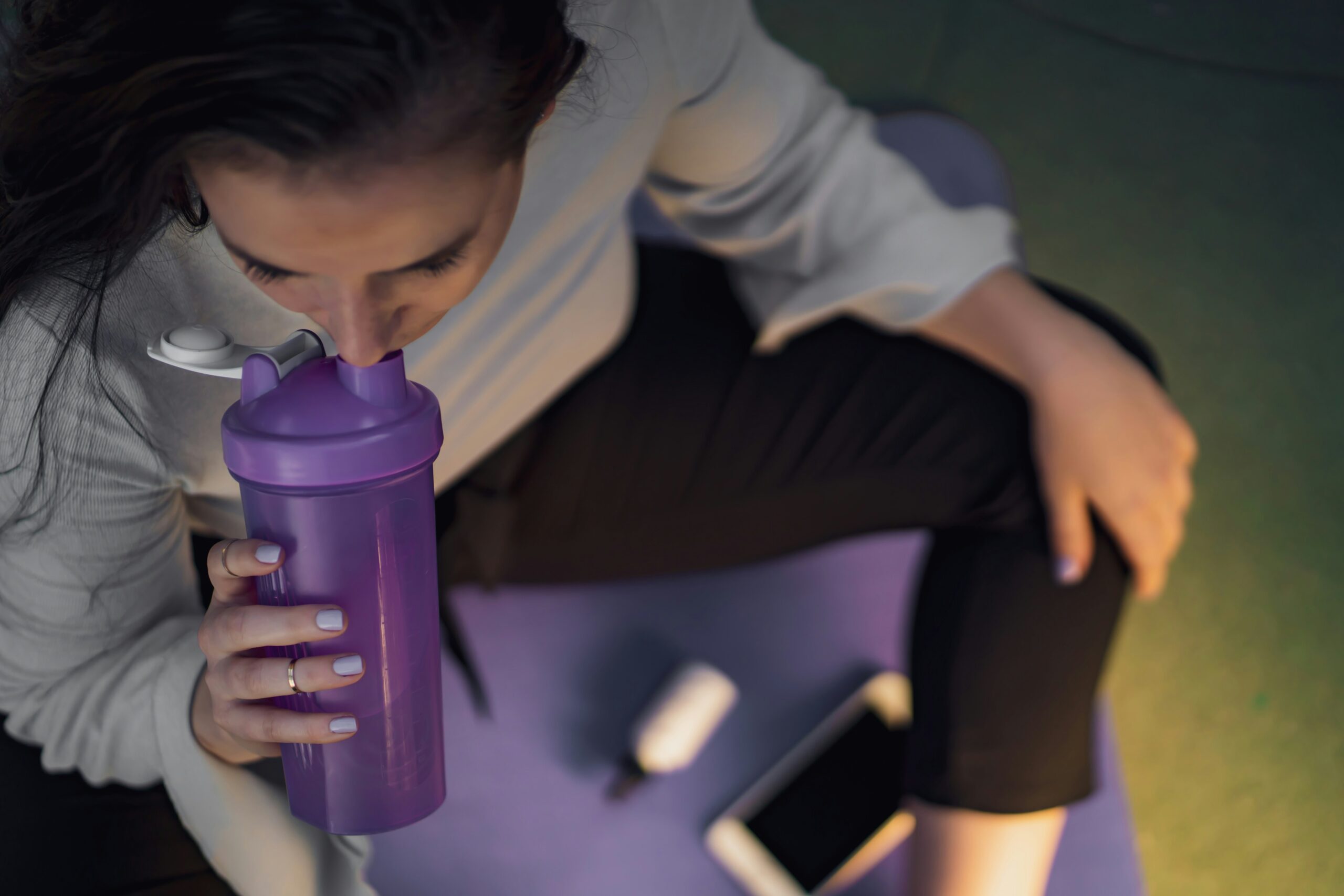 An athlete taking a capsule supplement with a water bottle after training